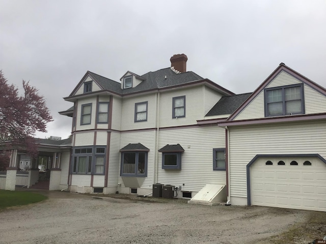 view of front of property featuring a garage, central AC, a chimney, and dirt driveway