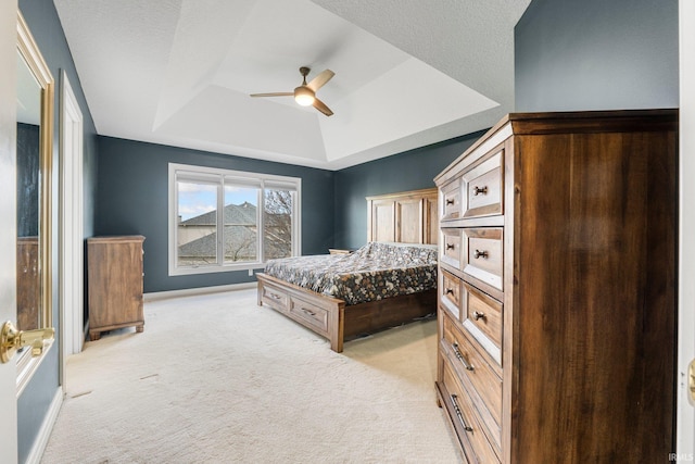 bedroom featuring light carpet, ceiling fan, baseboards, and a raised ceiling