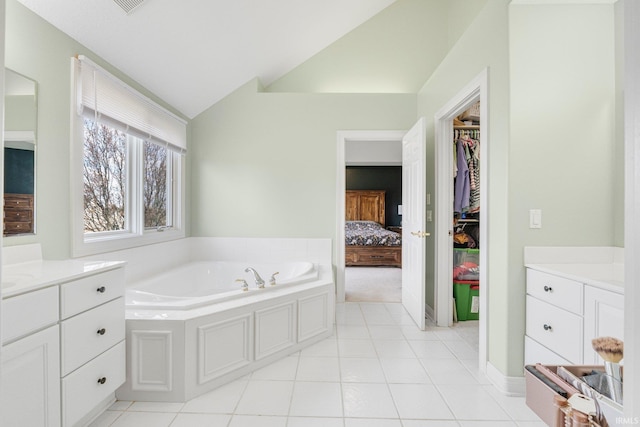 full bathroom with a garden tub, vanity, tile patterned flooring, vaulted ceiling, and a spacious closet