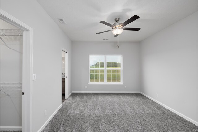 unfurnished bedroom with baseboards, carpet flooring, a walk in closet, visible vents, and ceiling fan