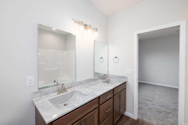 bathroom featuring a sink, baseboards, double vanity, and wood finished floors