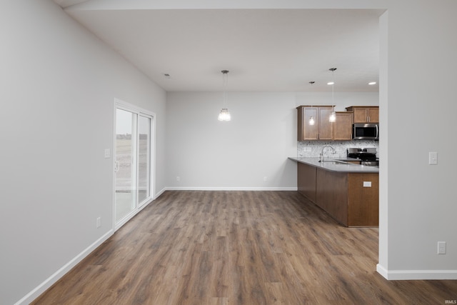 kitchen with a sink, appliances with stainless steel finishes, dark wood-style floors, brown cabinets, and decorative backsplash