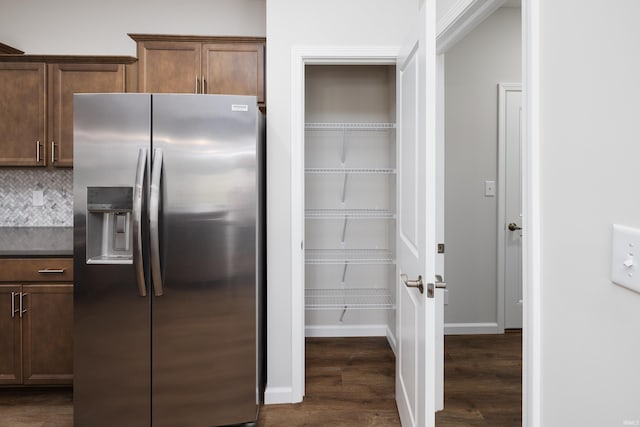 interior space featuring tasteful backsplash, dark wood-style flooring, dark countertops, stainless steel fridge, and baseboards