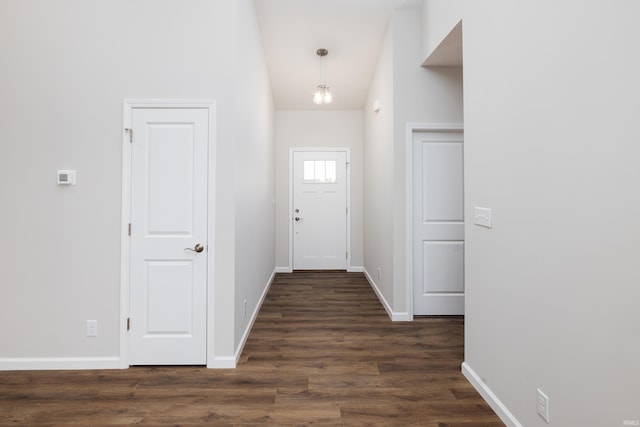 doorway with dark wood-style floors, baseboards, and vaulted ceiling