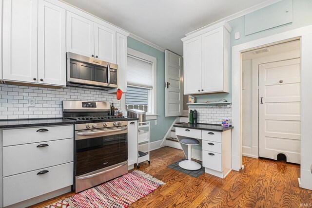 1069 Riverside Dr, South Bend, IN 46616 - kitchen featuring white cabinets, dark countertops, wood finished floors, stainless steel appliances, and decorative backsplash