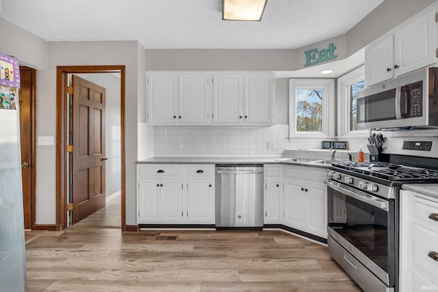 kitchen featuring tasteful backsplash, light wood finished floors, white cabinetry, and stainless steel appliances