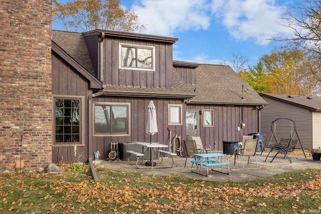back of property featuring board and batten siding, a chimney, a shingled roof, and a patio area