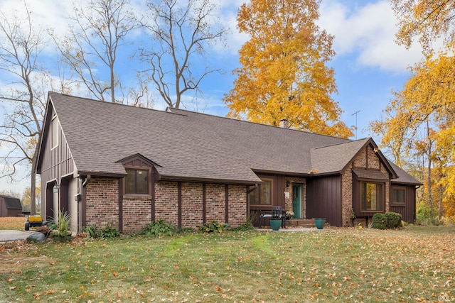 view of front of home with a chimney, board and batten siding, brick siding, a front lawn, and roof with shingles
