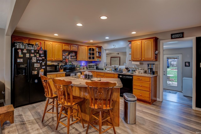 kitchen featuring a breakfast bar, black appliances, recessed lighting, light wood-style flooring, and a kitchen island