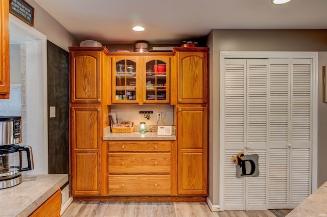 kitchen with glass insert cabinets, light countertops, brown cabinetry, and light wood-style flooring