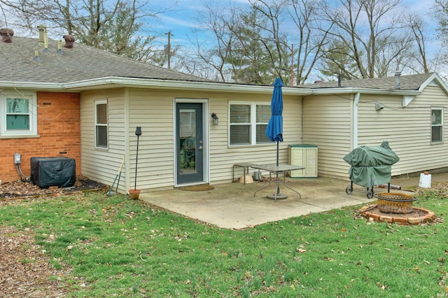 rear view of house featuring a lawn, a patio, roof with shingles, and an outdoor fire pit