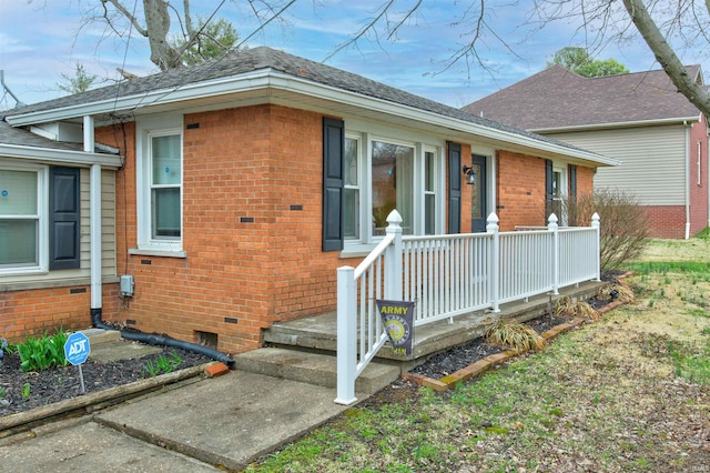view of front of house with roof with shingles, brick siding, and crawl space