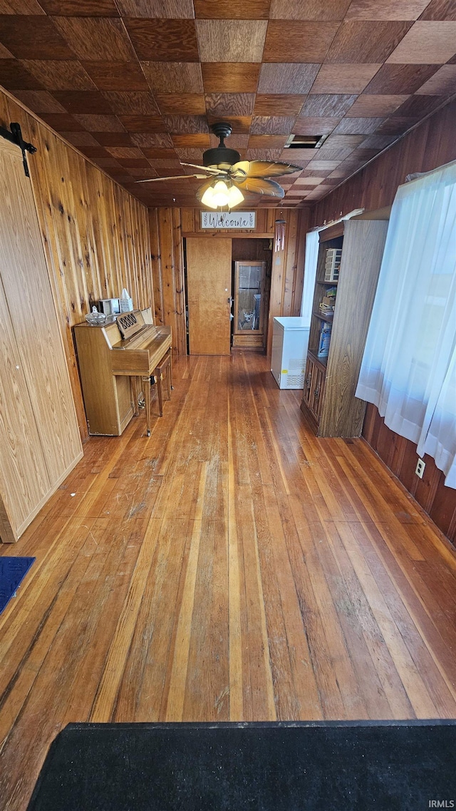 unfurnished living room featuring wood walls, ceiling fan, wood-type flooring, and visible vents
