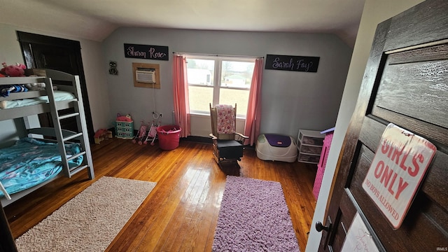 bedroom featuring a wall mounted AC, vaulted ceiling, and wood finished floors