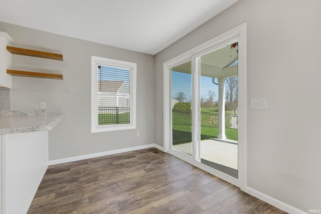 unfurnished dining area featuring baseboards, a healthy amount of sunlight, and dark wood-style floors