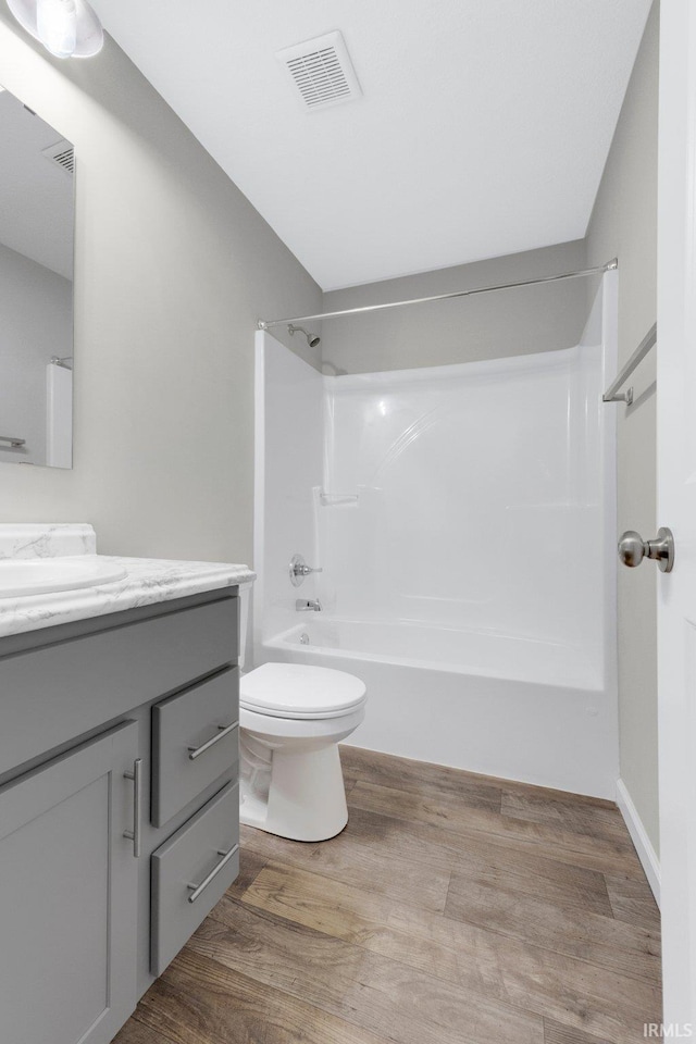 bathroom with wood finished floors, visible vents, toilet, vanity, and tub / shower combination