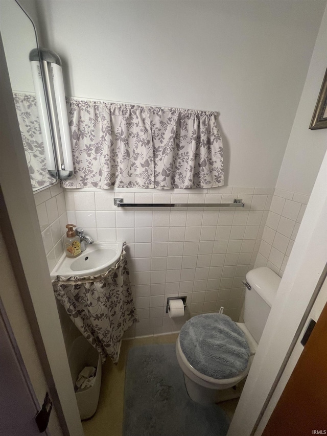 bathroom with wainscoting, tile walls, a sink, and toilet