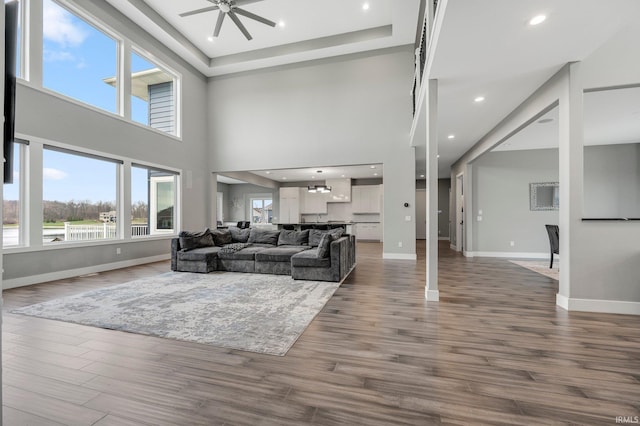 living room featuring a towering ceiling, dark wood-style flooring, baseboards, recessed lighting, and a ceiling fan