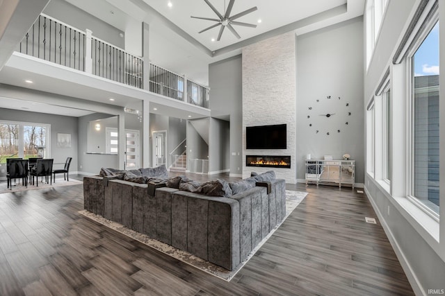 living area with a stone fireplace, baseboards, dark wood-style floors, a high ceiling, and a ceiling fan