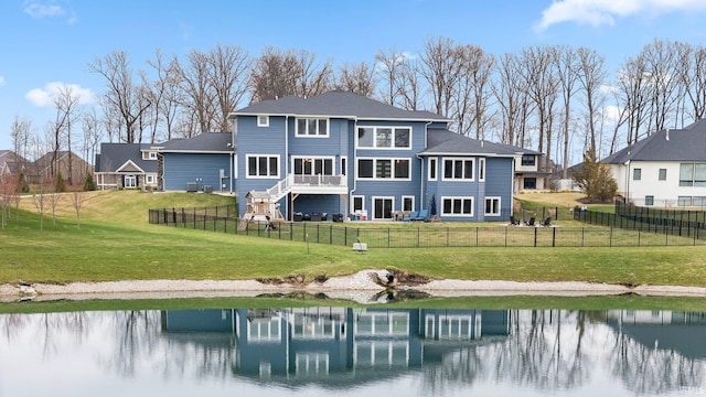 back of property with a water view, fence private yard, and a lawn
