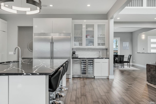 kitchen with white cabinetry, recessed lighting, wood finished floors, beverage cooler, and built in fridge