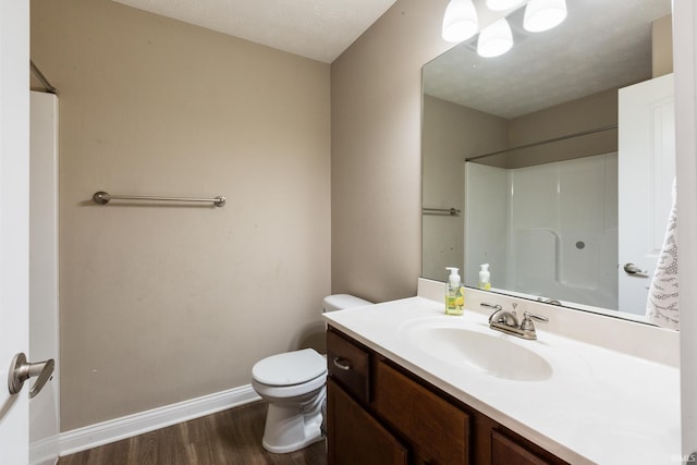 bathroom featuring baseboards, toilet, a shower, vanity, and wood finished floors