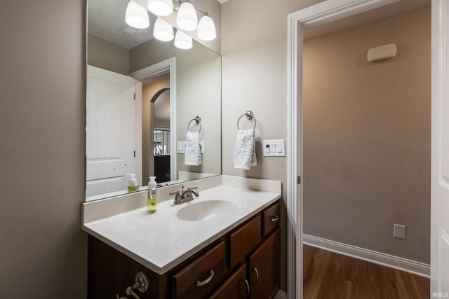 bathroom featuring a notable chandelier, vanity, baseboards, and wood finished floors