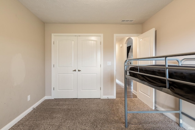 unfurnished bedroom with arched walkways, a closet, carpet flooring, and visible vents