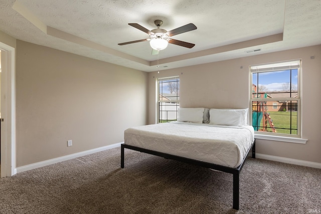 bedroom with baseboards, ceiling fan, carpet, a textured ceiling, and a tray ceiling