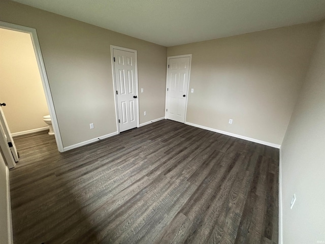 unfurnished bedroom featuring baseboards, connected bathroom, and dark wood finished floors