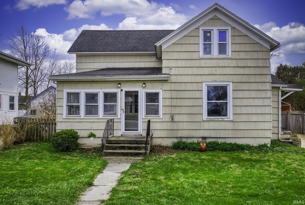 view of front facade with a front yard, fence, and a shingled roof