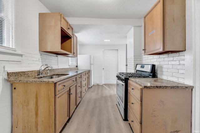 kitchen featuring gas range, a sink, freestanding refrigerator, light wood finished floors, and decorative backsplash