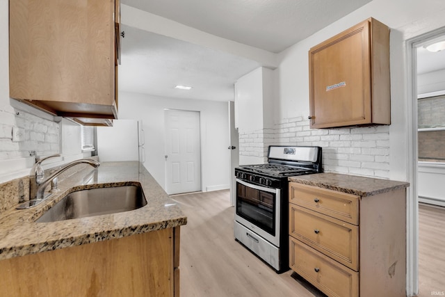 kitchen featuring backsplash, stainless steel range with gas cooktop, freestanding refrigerator, light wood-style floors, and a sink
