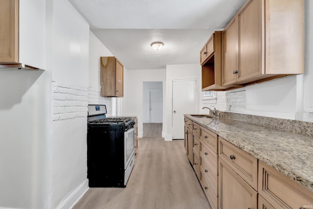 kitchen with stainless steel gas range, baseboards, light stone countertops, light wood-style floors, and a sink