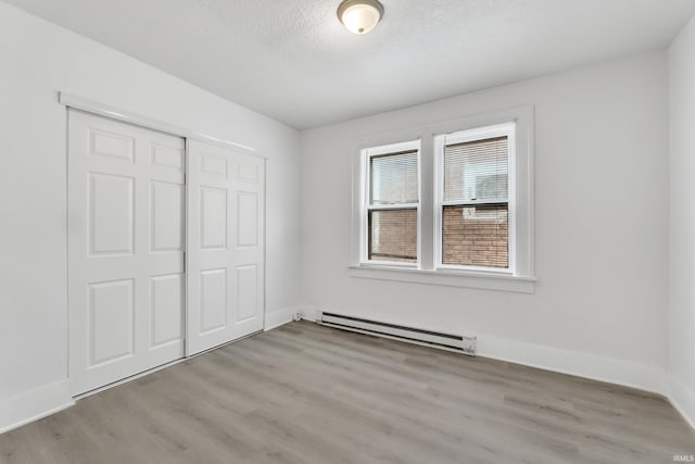 unfurnished bedroom with a textured ceiling, a closet, baseboard heating, wood finished floors, and baseboards