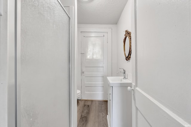 bathroom with a shower stall, a textured ceiling, vanity, toilet, and wood finished floors