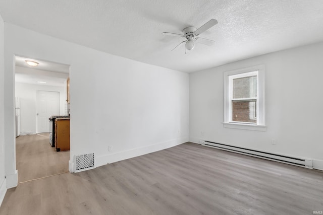 spare room with baseboard heating, a textured ceiling, visible vents, ceiling fan, and light wood finished floors