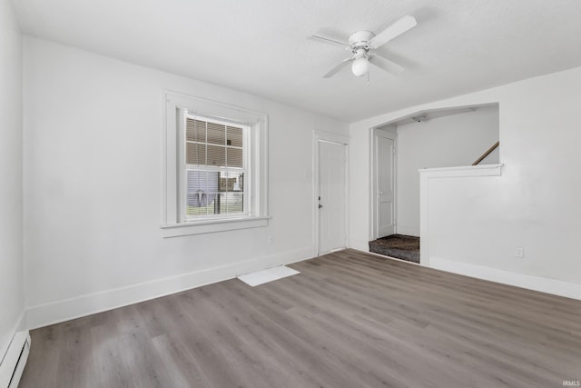 empty room with ceiling fan, a baseboard radiator, baseboards, and wood finished floors