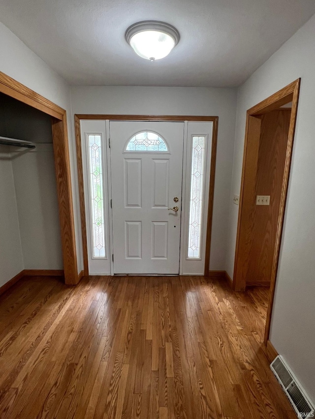 foyer entrance with baseboards, wood finished floors, and visible vents