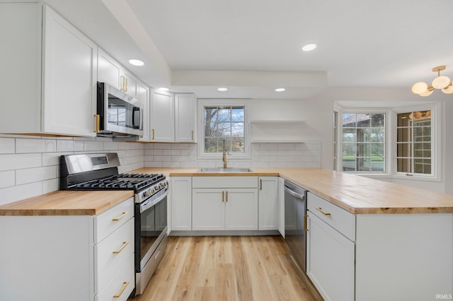 kitchen with a peninsula, open shelves, a sink, stainless steel appliances, and wood counters