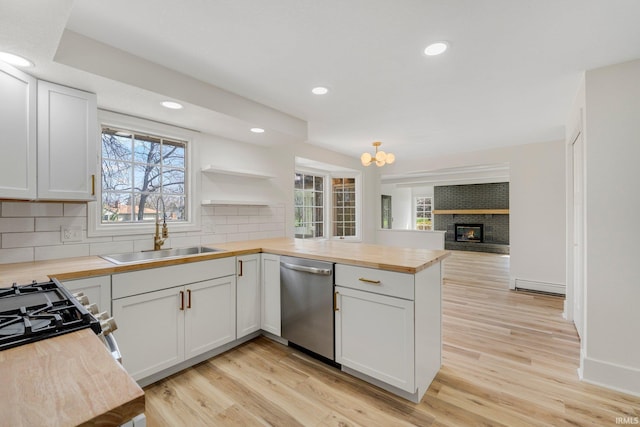 kitchen featuring butcher block countertops, a peninsula, backsplash, dishwasher, and a sink