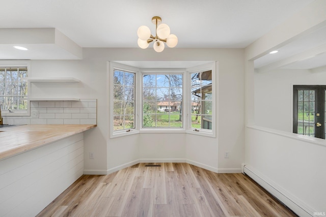 unfurnished dining area featuring a notable chandelier, baseboard heating, and a healthy amount of sunlight