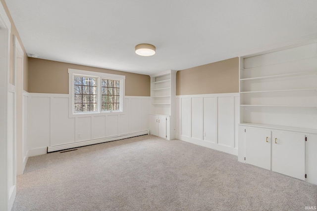 unfurnished room featuring a decorative wall, carpet floors, a baseboard radiator, and wainscoting