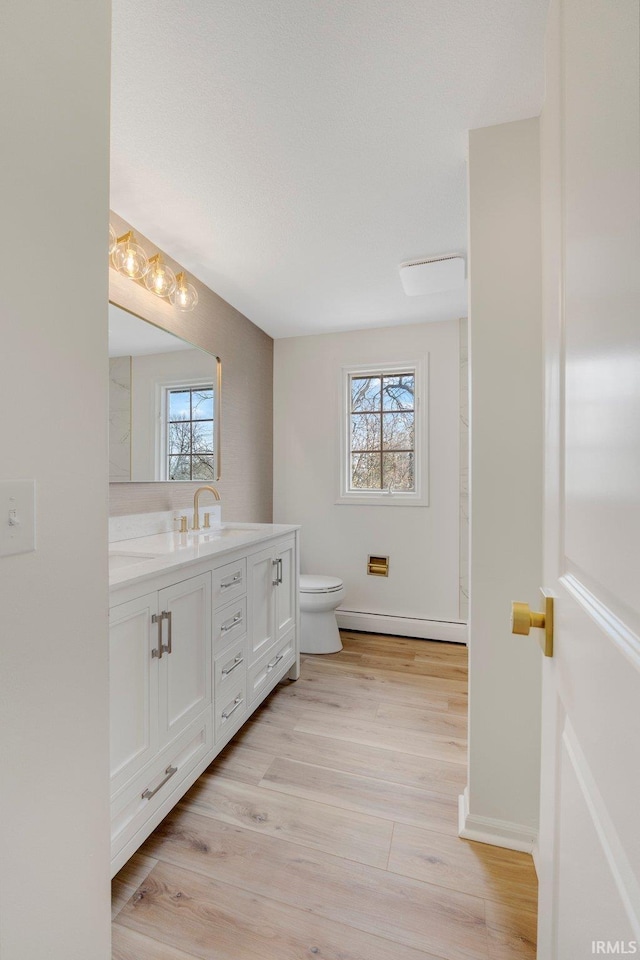 bathroom featuring plenty of natural light, vanity, baseboard heating, and toilet