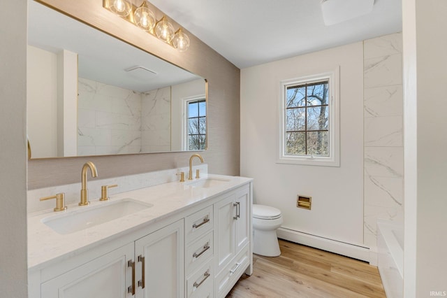 bathroom featuring toilet, a healthy amount of sunlight, a baseboard heating unit, and a sink