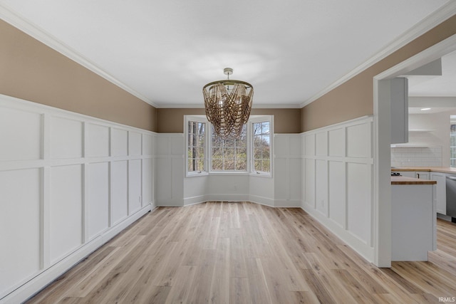 unfurnished dining area with light wood-style flooring, a decorative wall, a notable chandelier, and a wainscoted wall