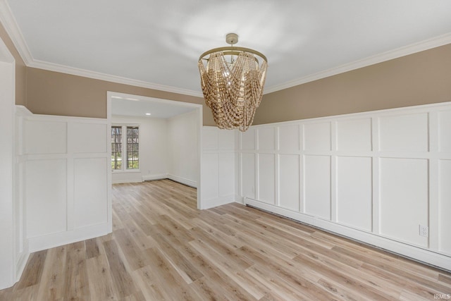 unfurnished dining area featuring a decorative wall, a chandelier, crown molding, wainscoting, and light wood-style flooring