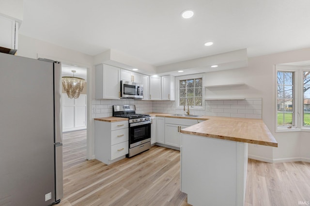 kitchen featuring butcher block countertops, light wood finished floors, open shelves, and stainless steel appliances