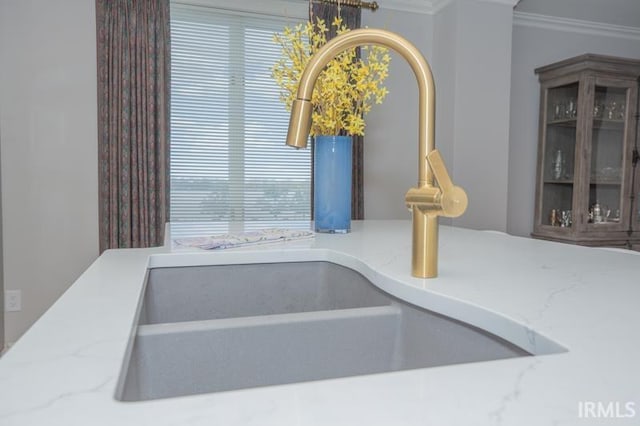 interior details featuring crown molding, a sink, glass insert cabinets, and light stone countertops