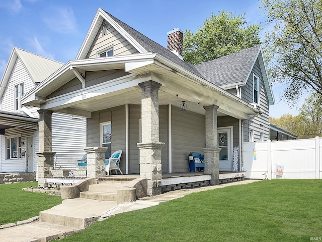 view of front of home featuring a chimney, covered porch, fence, and a front lawn